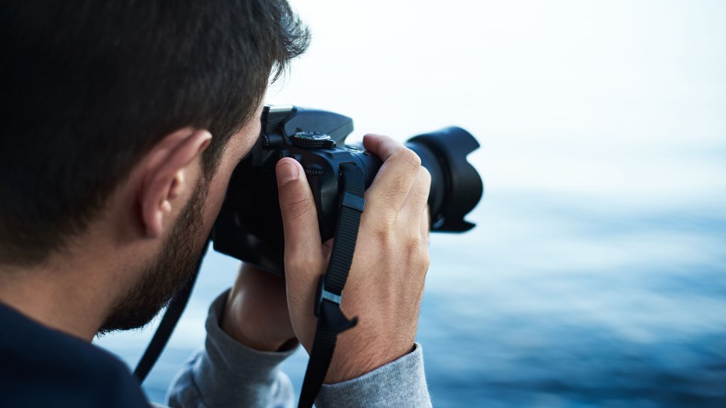 A Young Man Photographer With Digital Dslr Camera Reflex On Shore Lake Or Sea
