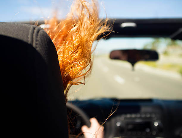 A woman with red hair driving a convertible vehicle on the open road.
